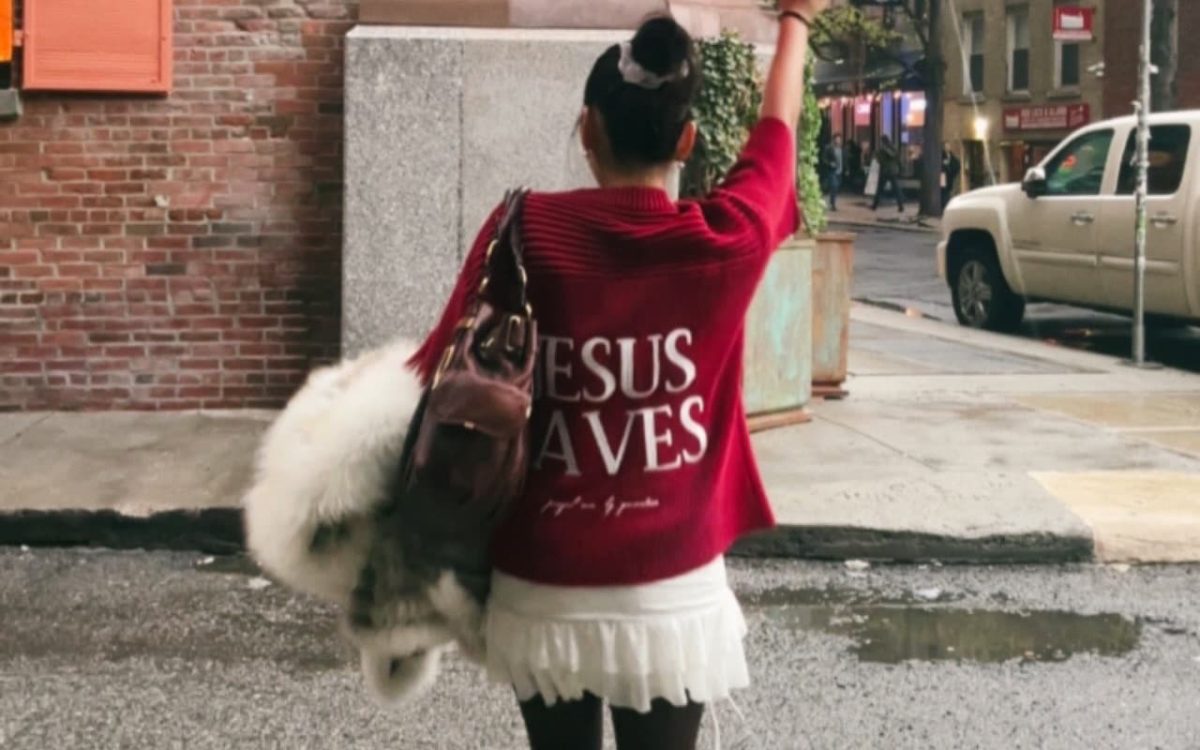 Mesmo em dias de chuva, a fé se manifesta. A mensagem "JESUS SAVES" (Jesus Salva) na blusa desta pessoa é um lembrete do poder transformador e da esperança que Cristo oferece.